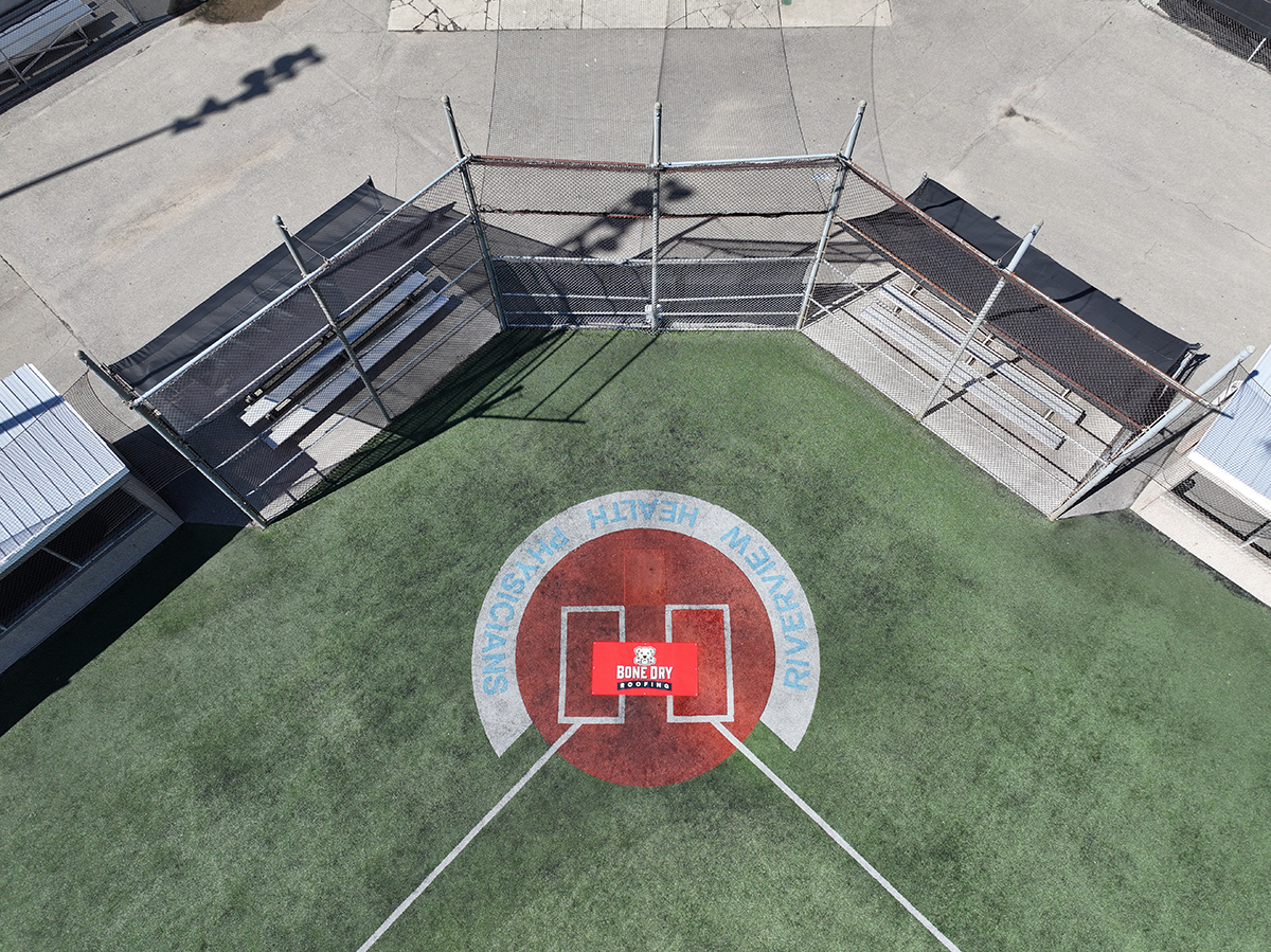 Baseball field_Little League with banner An overhead drone shot of home plate at a baseball diamond with the red Bone Dry Roofing logo