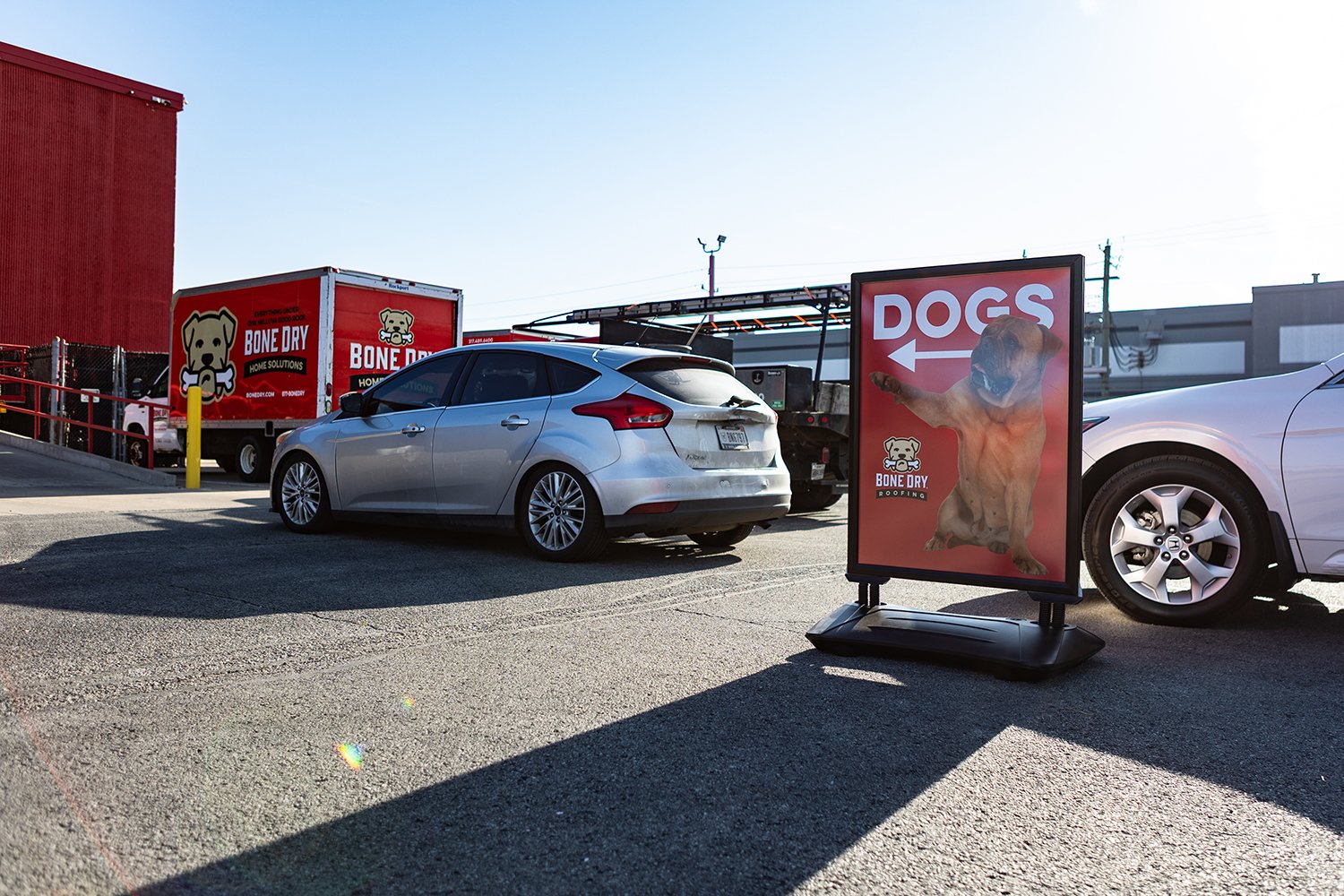 Indy Humane_11_5.10.2025_2 Cars drive into a warehouse. A red sign with a dog on it guides them.